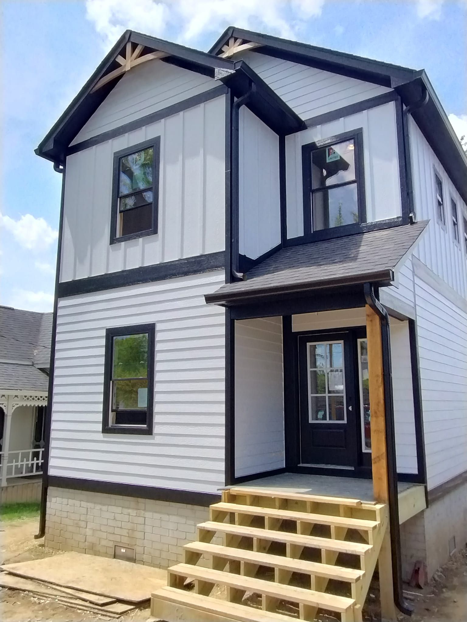 A white house with black trim and stairs is under construction.