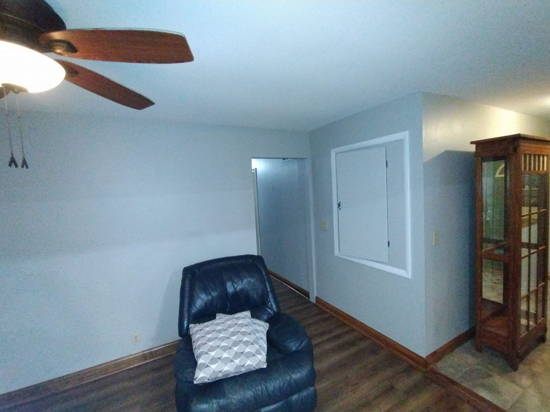 A living room with a chair , ceiling fan , and glass cabinet.
