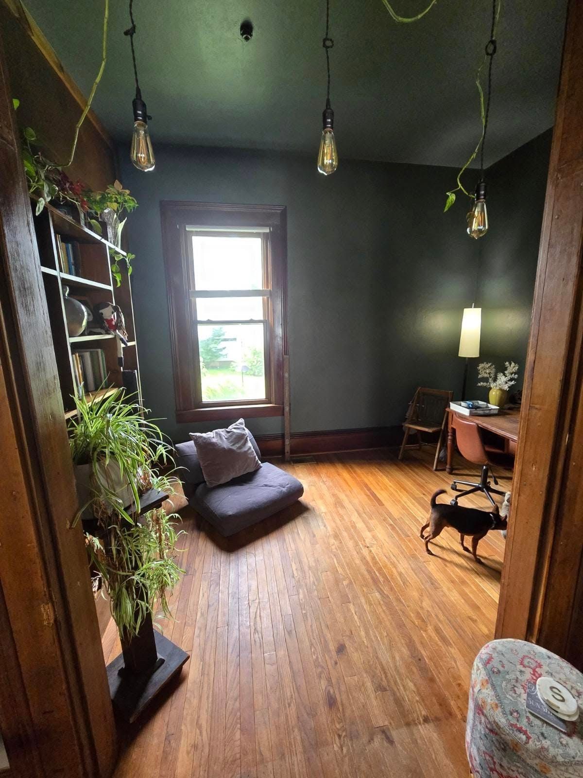 A living room with hardwood floors , a couch , a desk and a window.