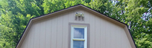 The roof of a barn with a window and trees in the background