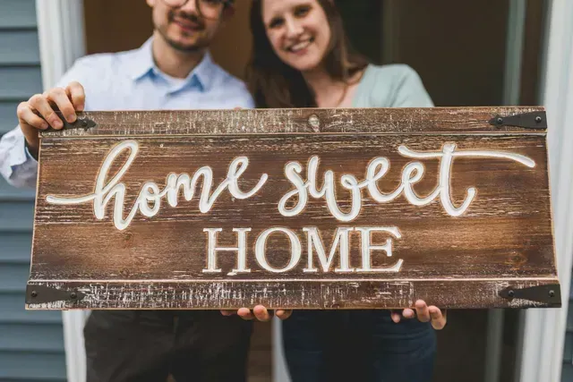 Couple holding a 'Home Sweet Home' sign in front of their newly rented pet-friendly house with fenced yard in Springfield, MO