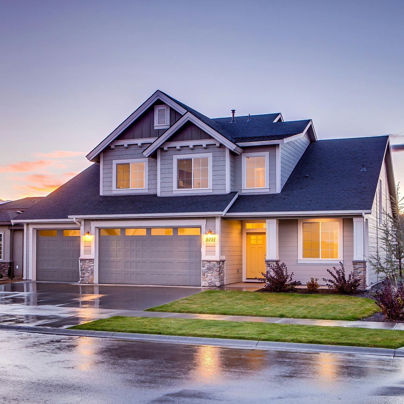 A large house with two garage doors and a sunset in the background