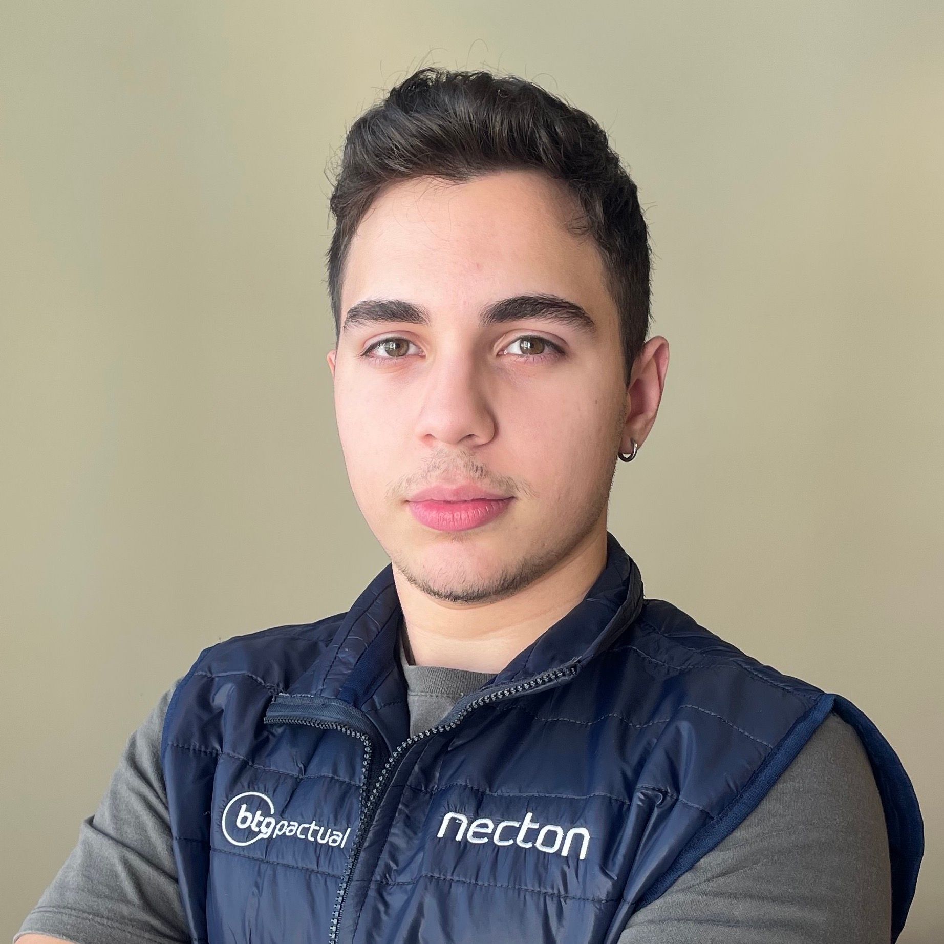 Homem vestindo um colete azul-marinho com o logotipo de uma empresa, olhando para a câmera com uma expressão neutra.