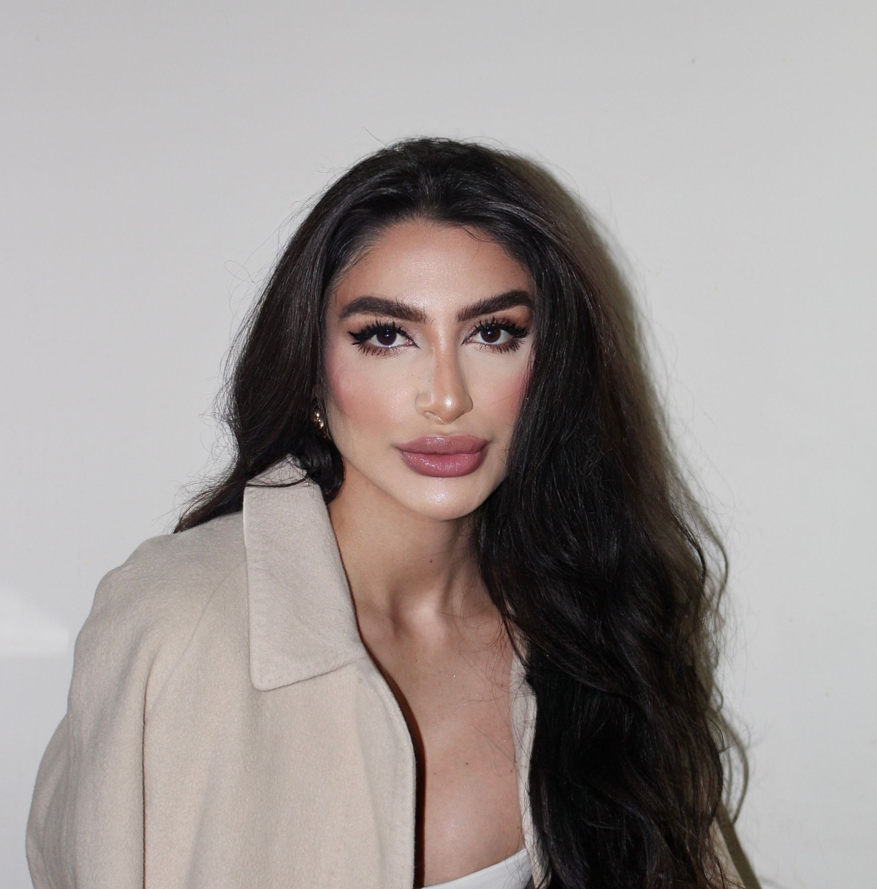 Mulher de blazer azul claro, sorrindo, com longos cabelos escuros e usando brincos de argola.