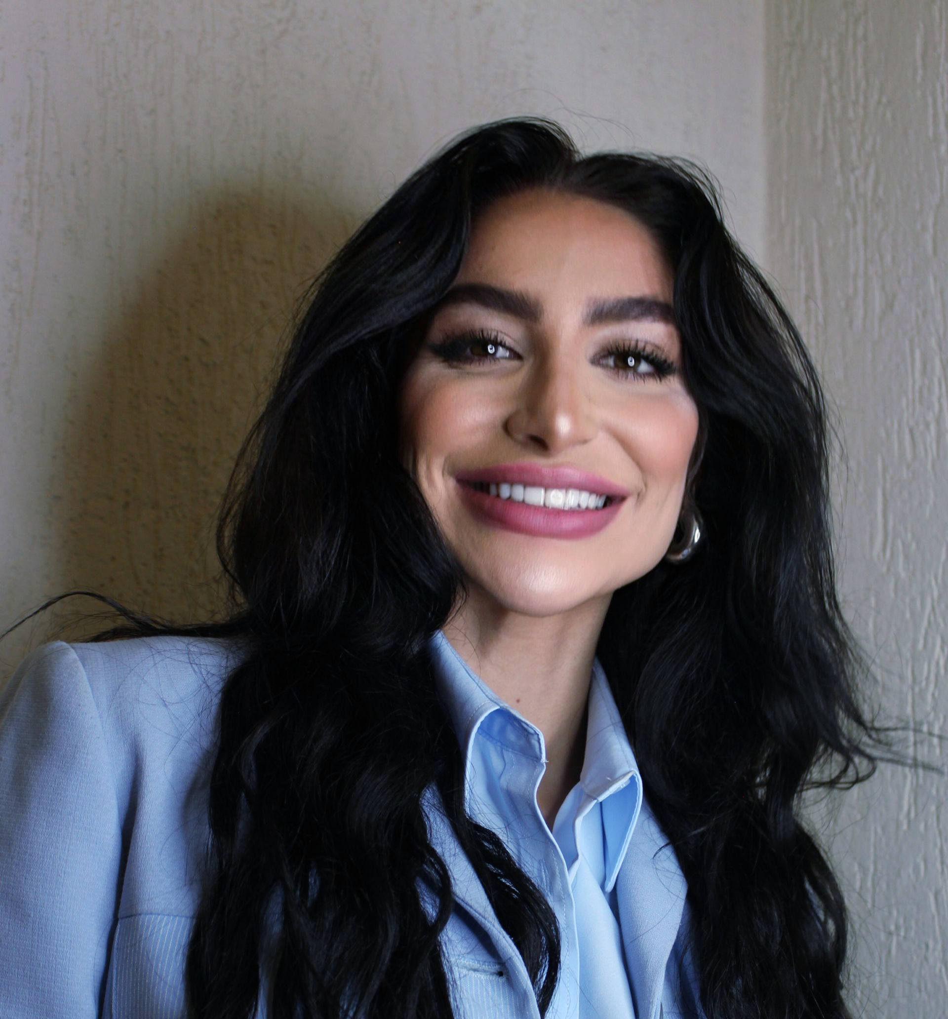 Mulher de cabelos escuros sorri, vestindo um blazer azul claro e uma camisa de colarinho.