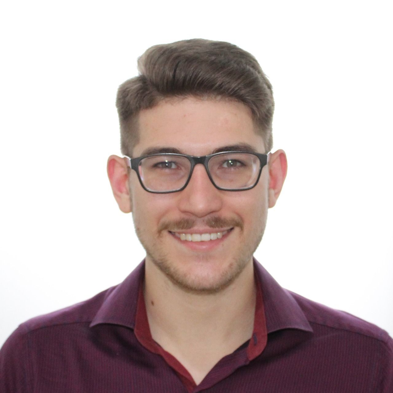 Homem de óculos e camisa bordô, sorrindo para a câmera.