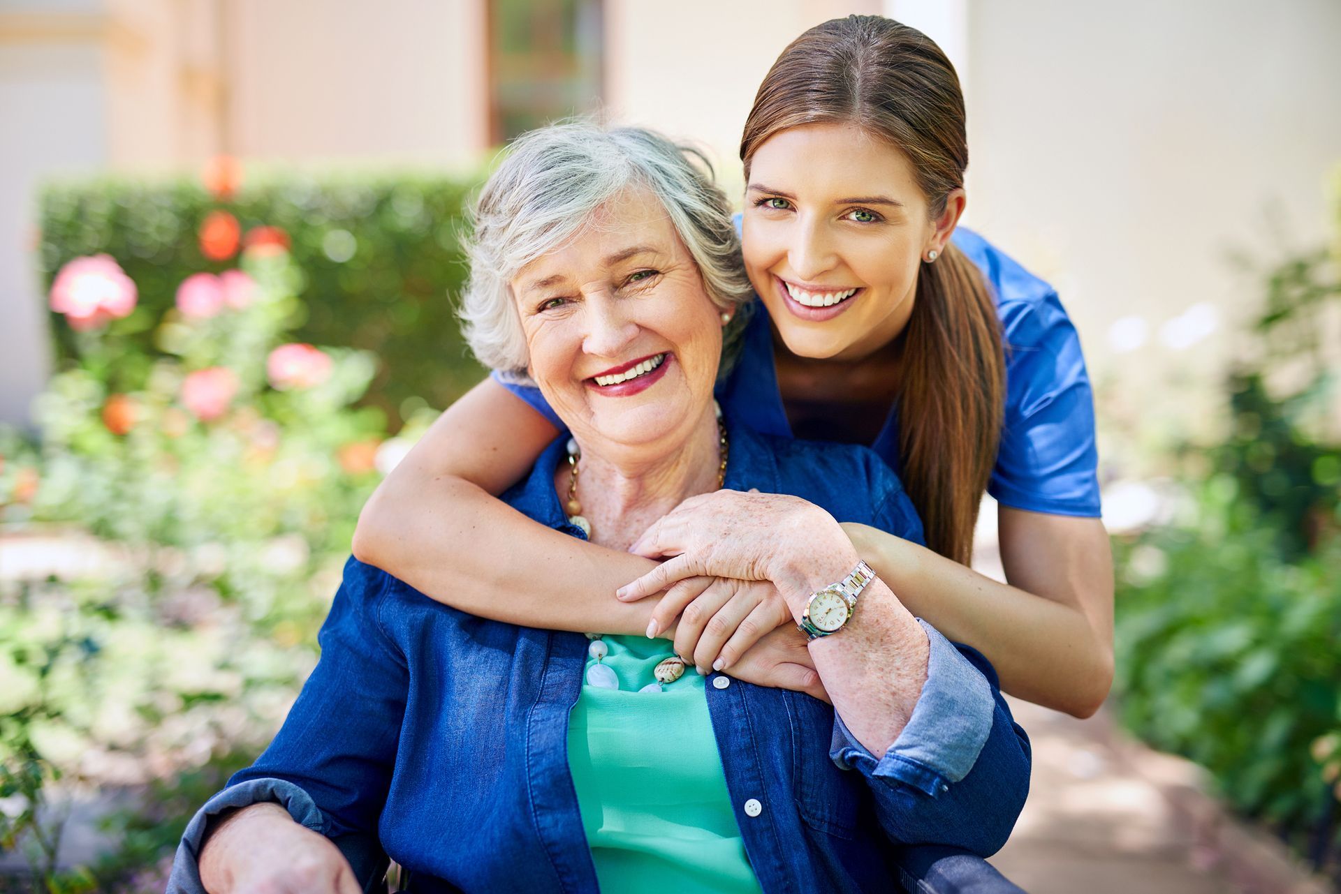 A young woman is hugging an older woman in a wheelchair.