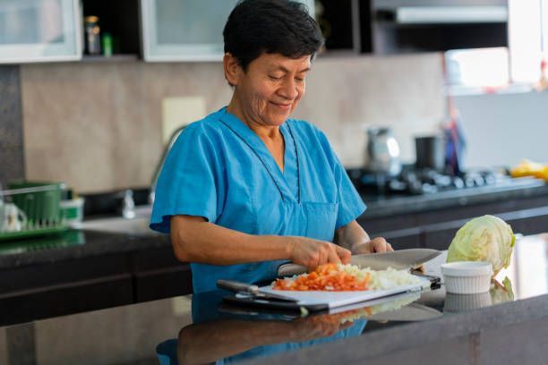 A woman in a blue scrub is cutting vegetables in a kitchen.