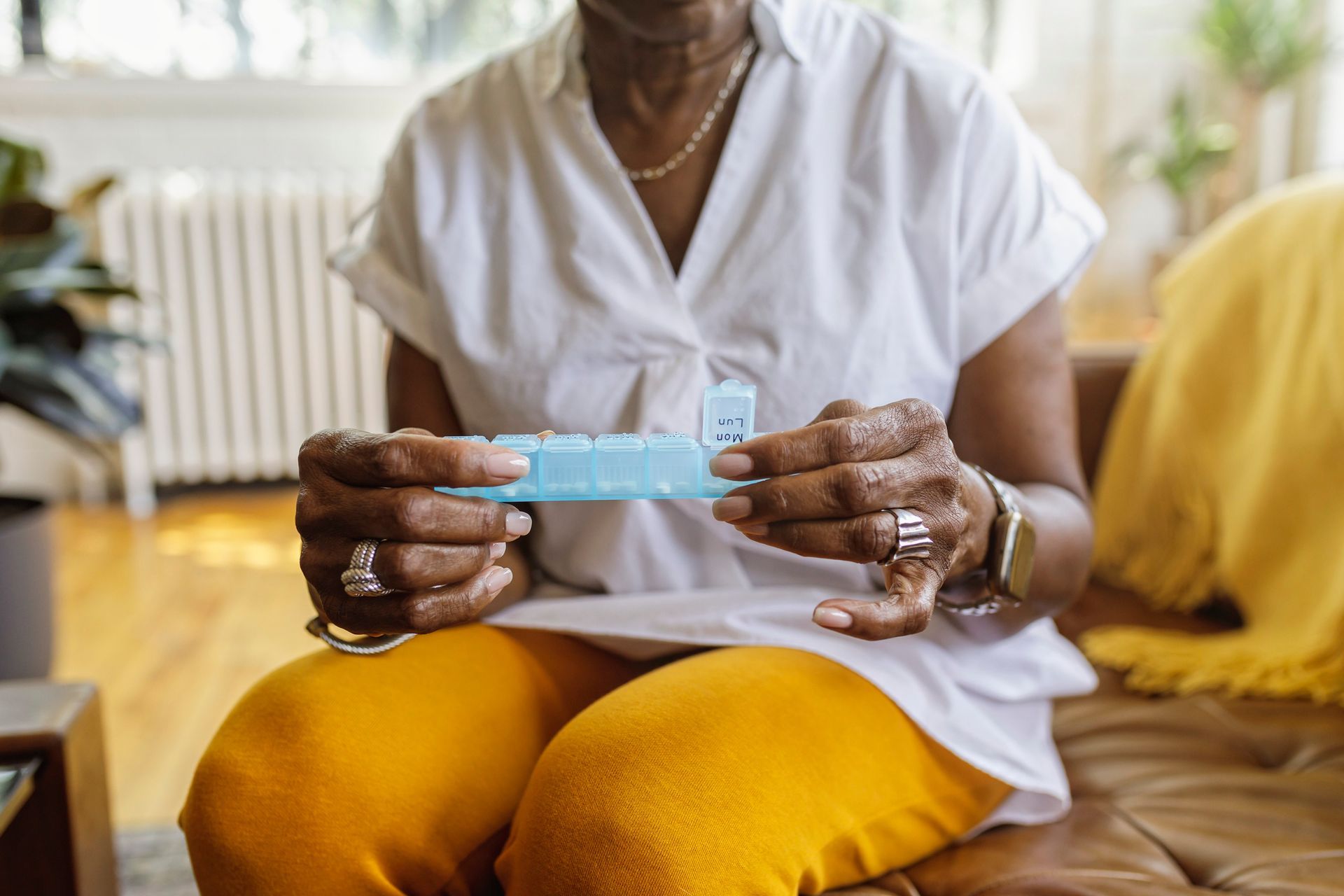 An elderly woman is sitting on a couch holding a pill box.