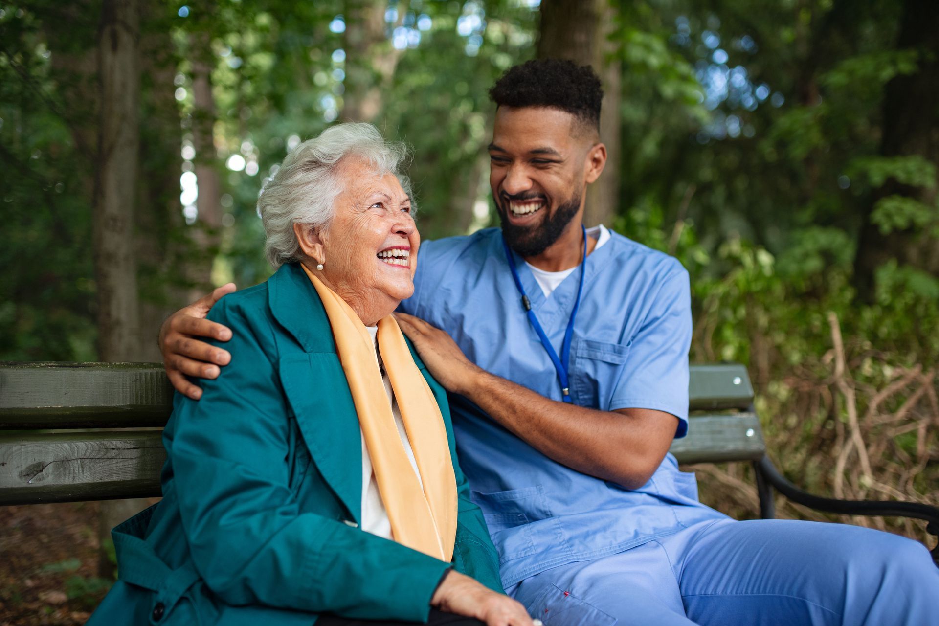 A nurse is sitting on a park bench with an elderly woman.