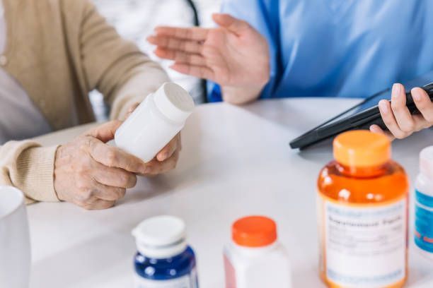 A doctor is talking to an elderly woman while she holds a bottle of pills.