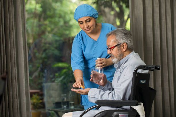A nurse is giving an elderly man in a wheelchair a pill.