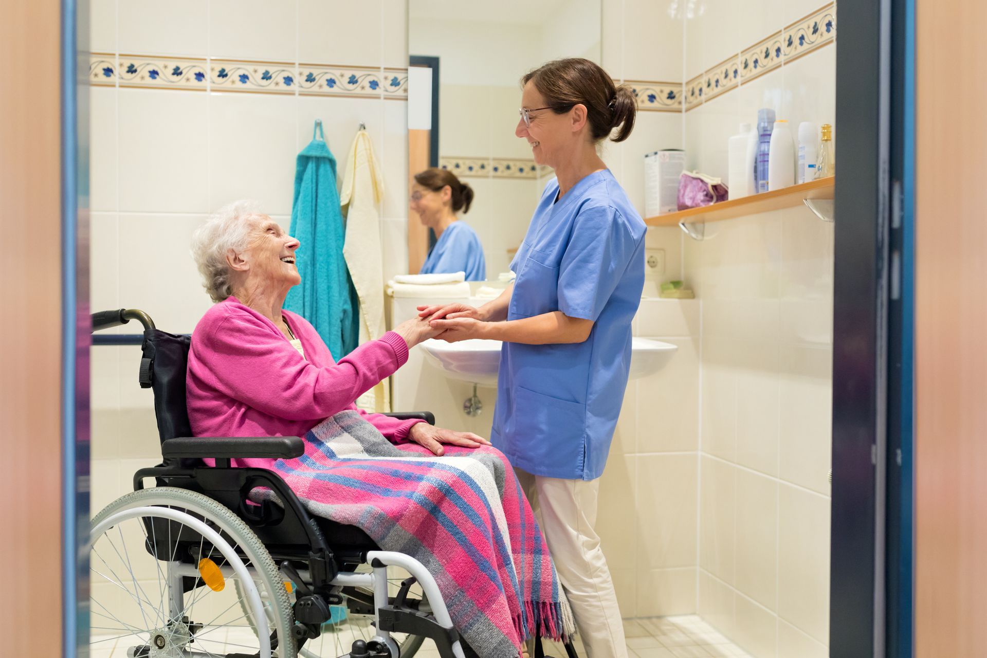 An elderly woman in a wheelchair is talking to a nurse in a bathroom.