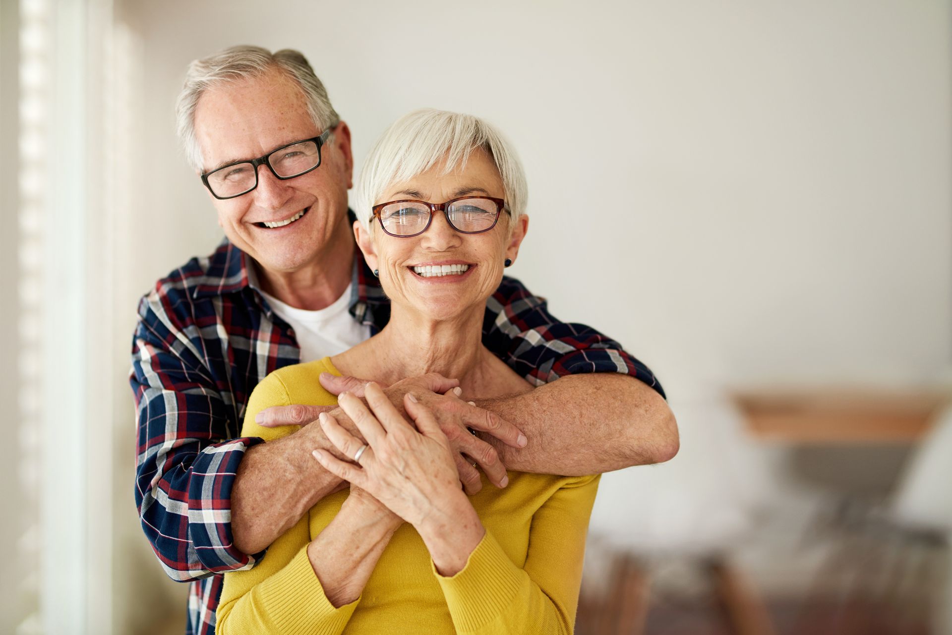 An elderly couple is hugging each other and smiling for the camera.
