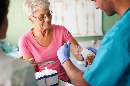 An elderly woman is getting her wrist bandaged by a doctor.