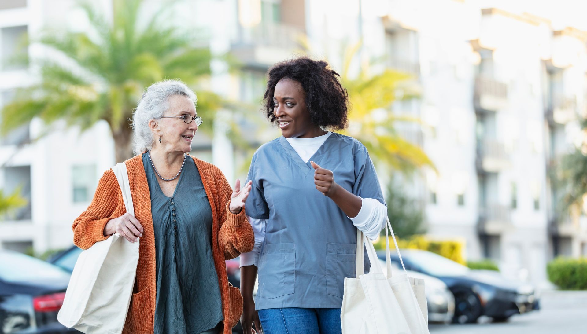A nurse is helping an elderly woman walk down the street.