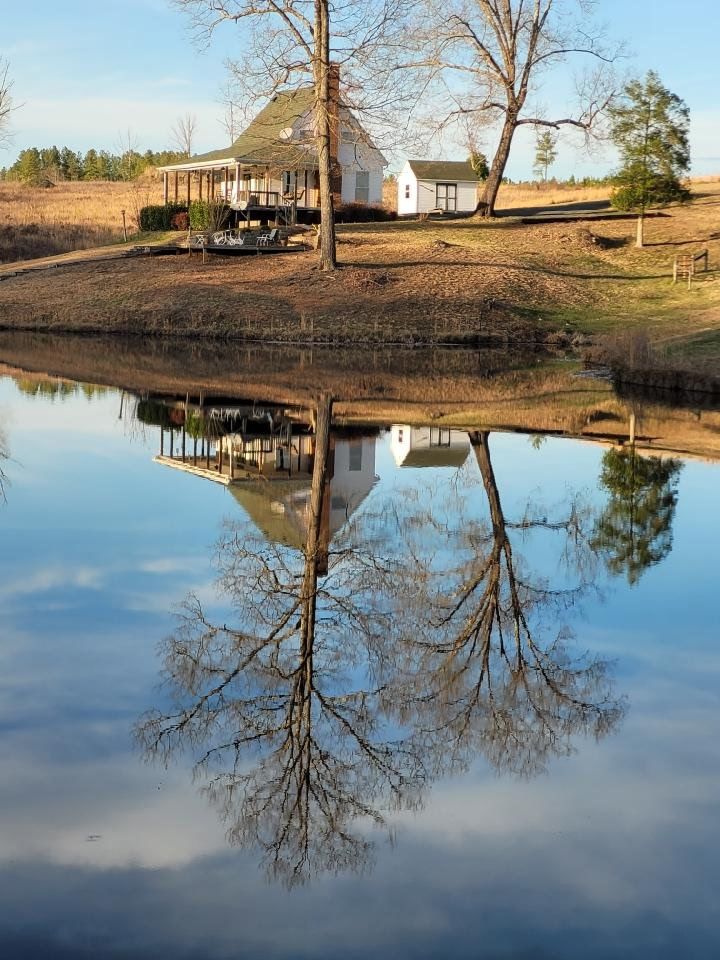 White house and trees reflected in a still pond. Blue sky and brown landscape.
