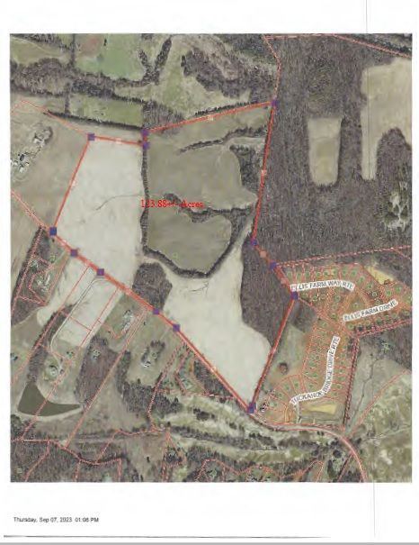 Aerial view of a plot of land outlined in red with surrounding residential areas and forested areas.