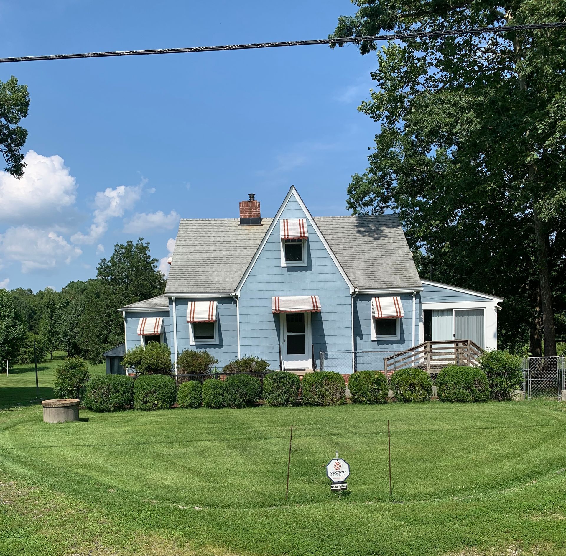 Blue house with white trim, small yard, blue sky, and green foliage.