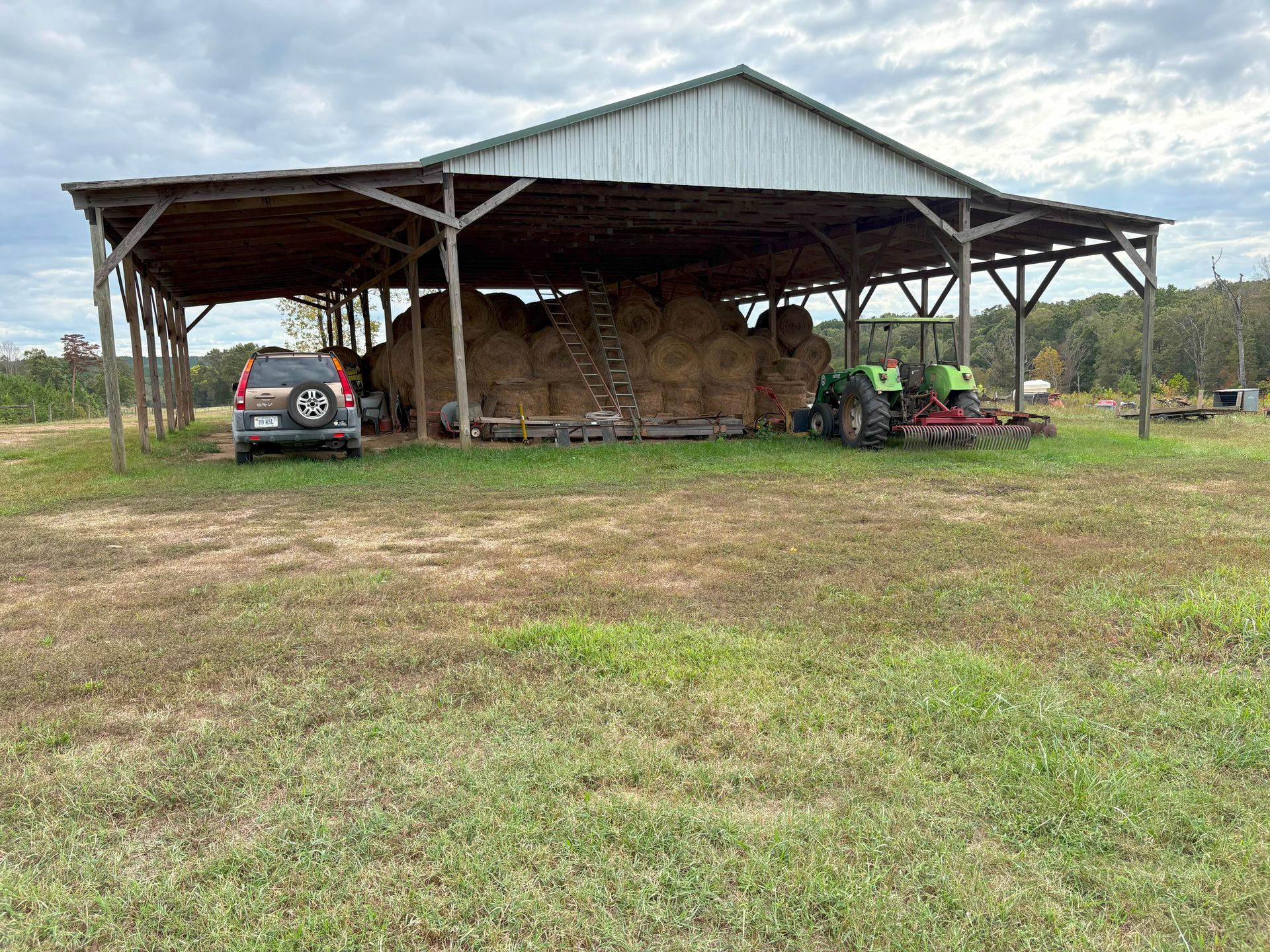 Barn filled with hay bales, car, and tractor under a cloudy sky.