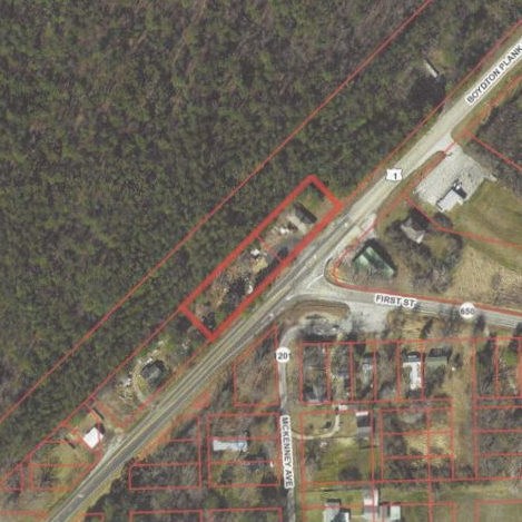 Aerial view of a road intersection in a rural area, with houses and wooded areas visible.