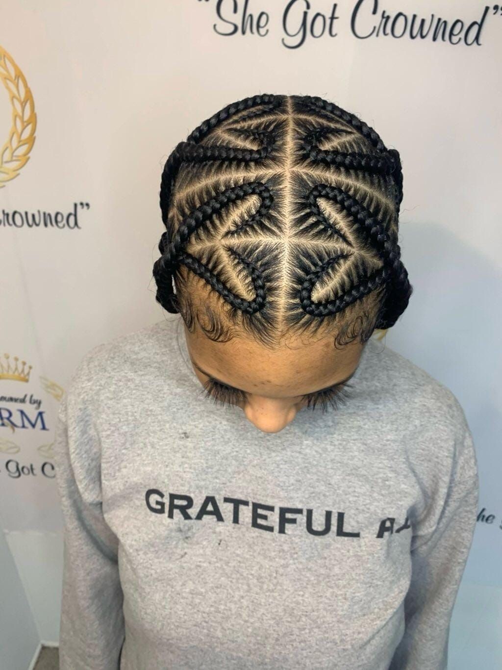 A person with dark hair styled in intricate, symmetrical cornrows forming a geometric, star-like pattern on their scalp.