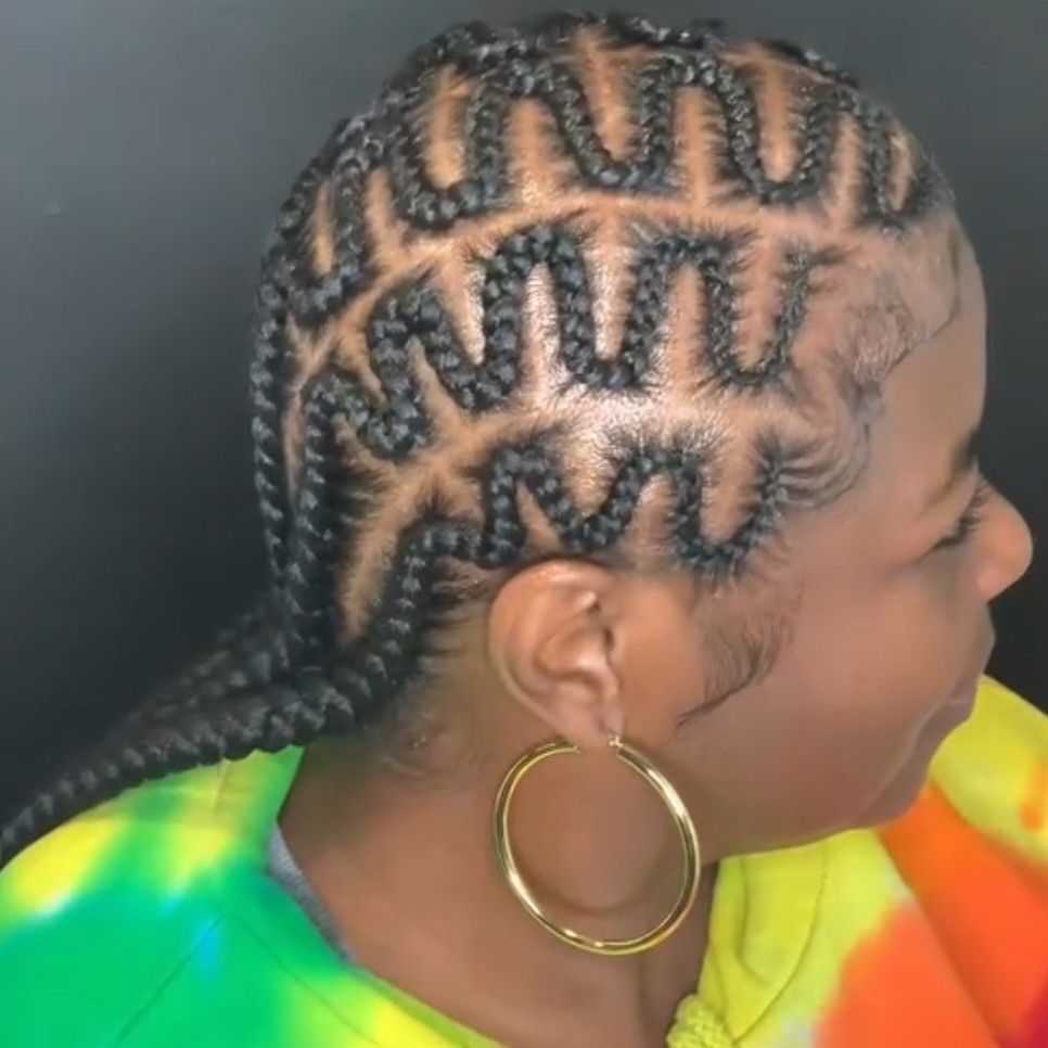 A profile view of a hairstyle featuring tight, zigzag cornrow braids parted in clean geometric sections.