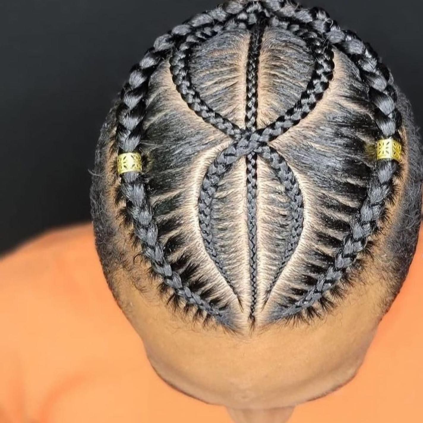 Close-up view of hair braided into an infinity-shaped design on the scalp, accented with two small gold hair cuffs.