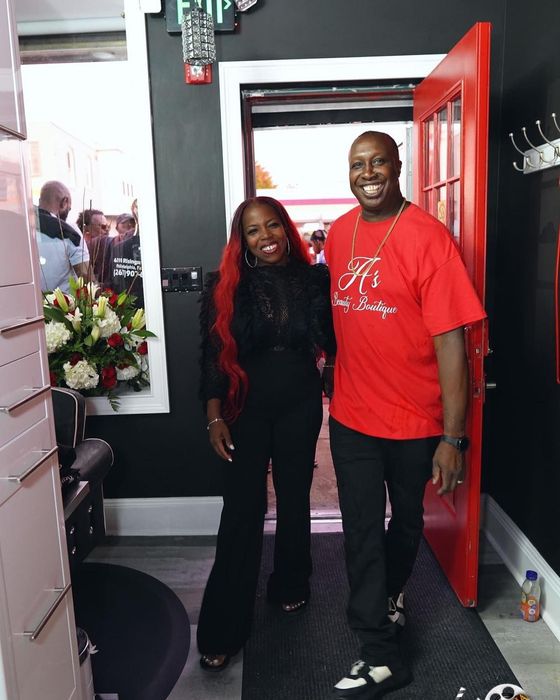 A woman with long red hair and a man in a red shirt stand smiling side-by-side in a doorway.