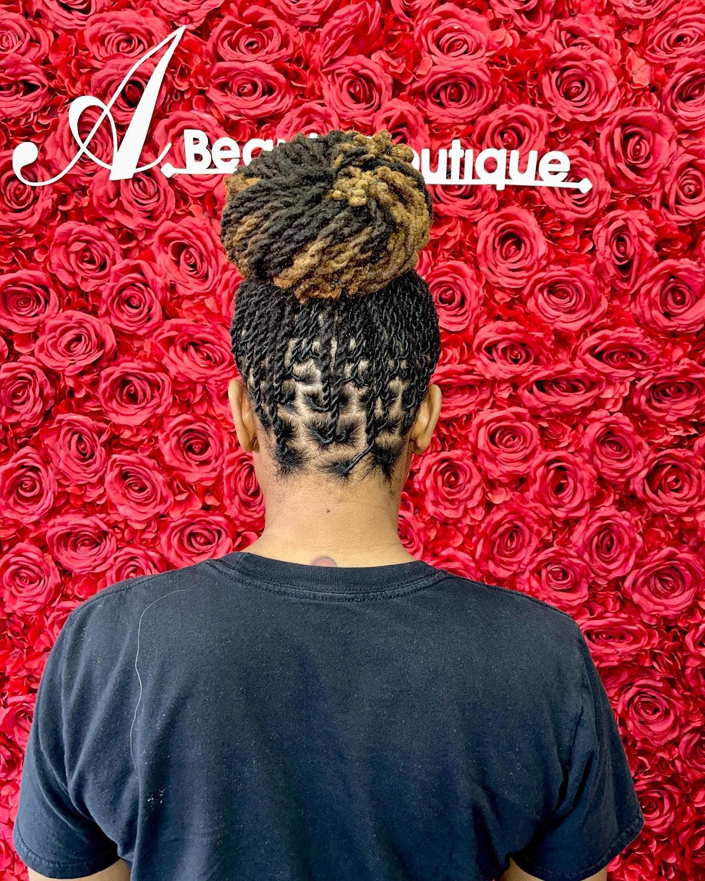 A person with dreadlocks styled in a high bun stands in front of a red rose wall with a beauty salon sign.