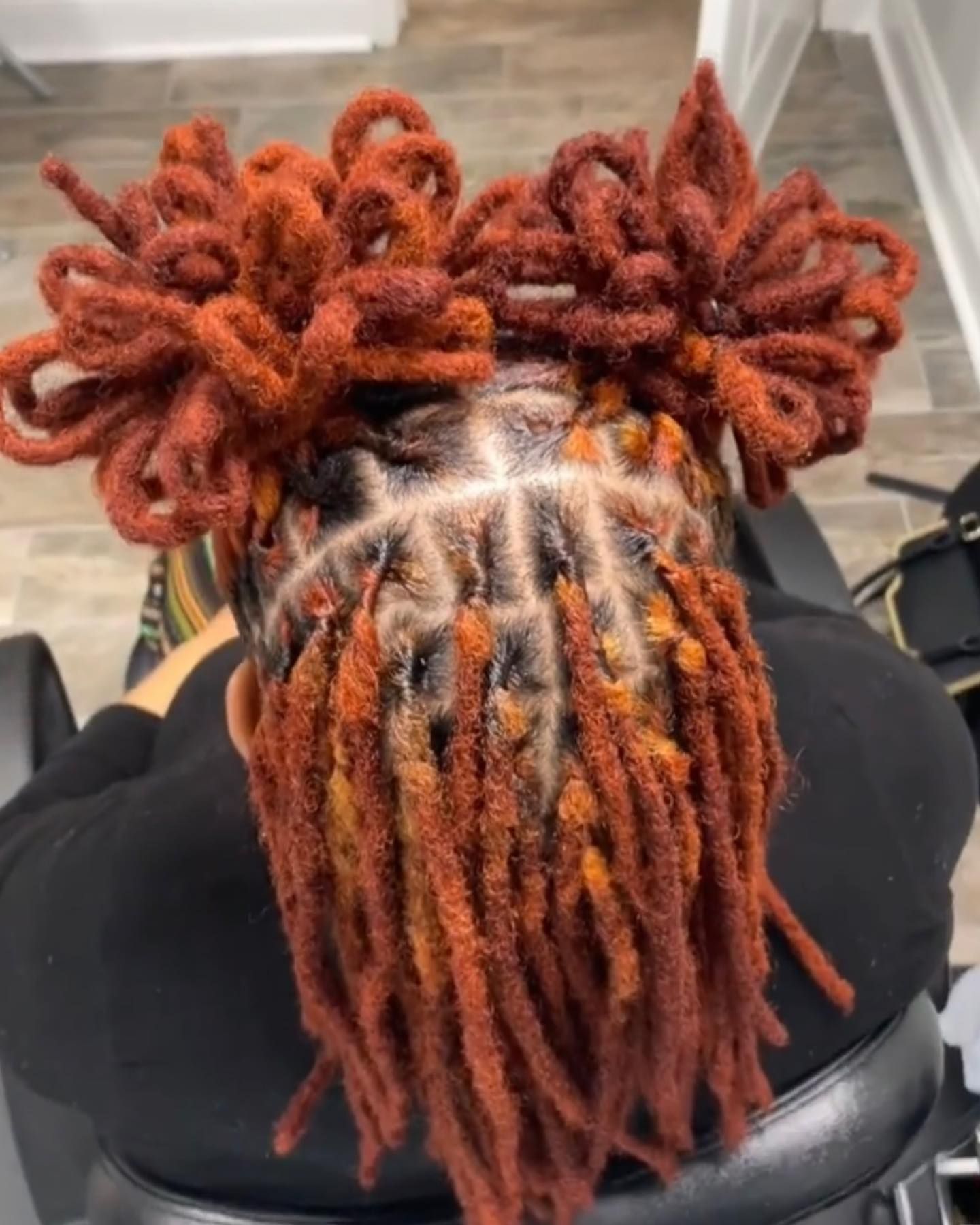 Red-brown dreadlocks styled in two top buns and loose hanging locs with neatly parted, defined roots.