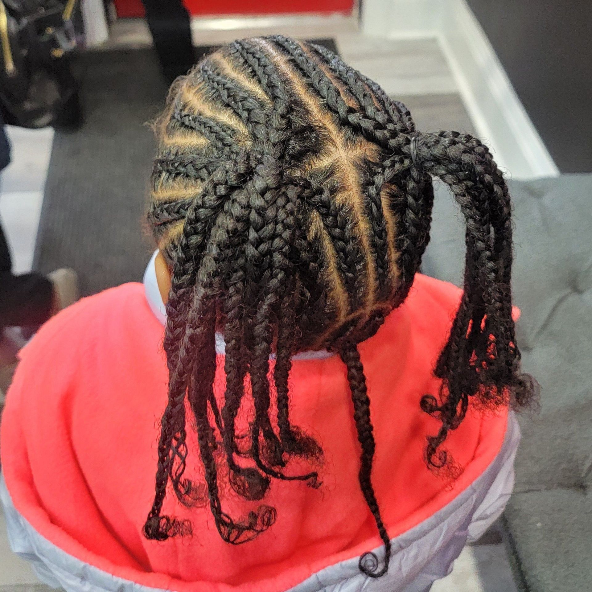 A person with dark hair styled in cornrow braids parted into two high pigtails, wearing a red and grey hooded jacket.