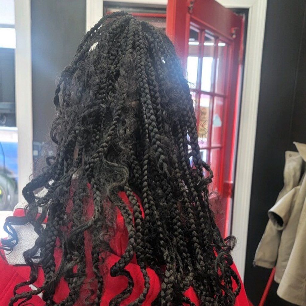 A person wearing long black braided hair with wavy, loose ends, styled partially up and falling down their back.