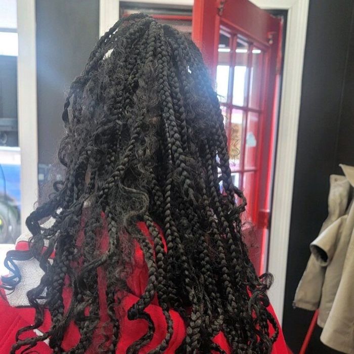 A person with dark, braided hair with wavy, loose ends, viewed from behind, standing near a red-framed door.