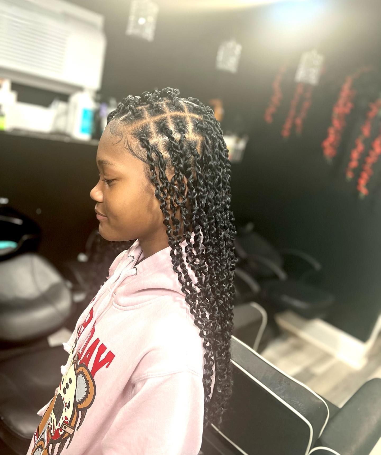 A person with a butterfly loc hairstyle featuring a grid-patterned scalp design, viewed from the side in a salon.