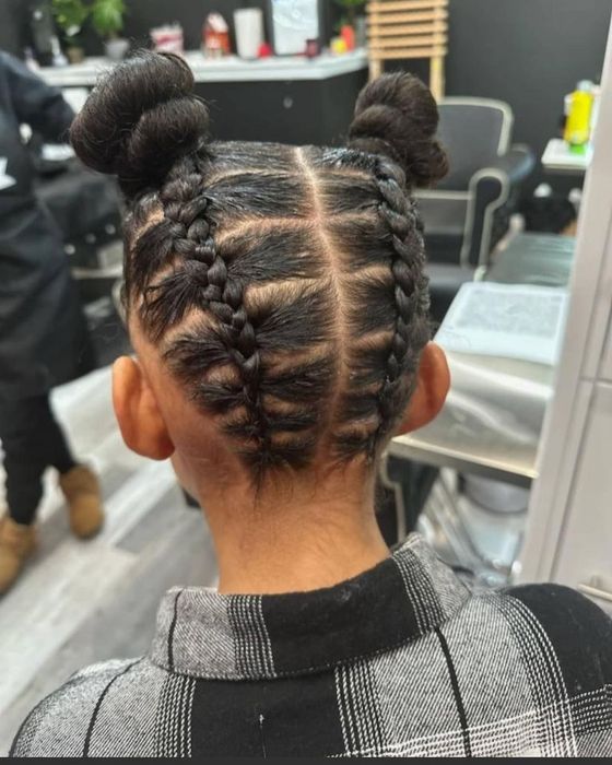 Back view of a person with dark hair styled in two cornrow braids leading into two neat high buns in a salon setting.