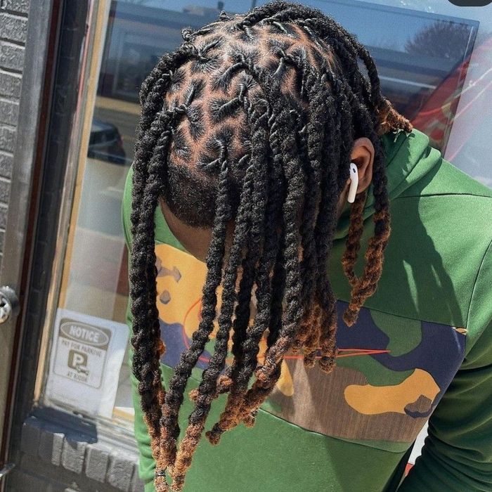 A person wearing a green camo hoodie with shoulder-length, dark brown twists featuring lighter, auburn-colored ends.