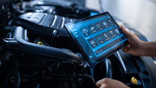 A person is using a tablet to check the engine of a car.