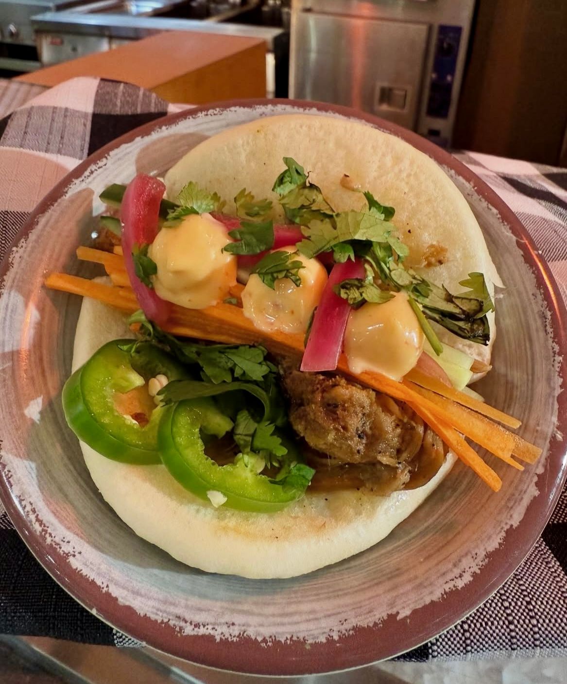 Bao bun with filling: meat, carrots, pickled onions, jalapenos, and sauce, on a plate.