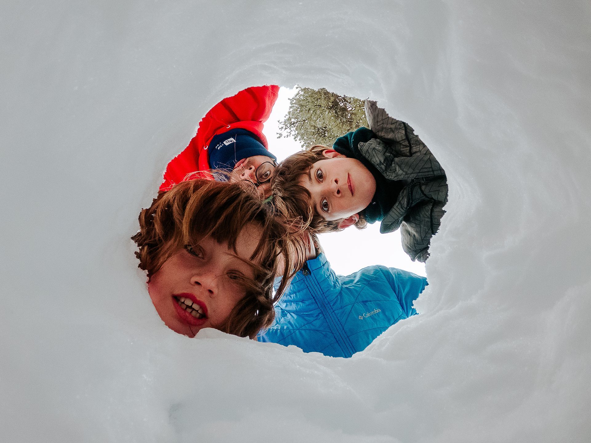 Three children are looking out of a hole in the snow.