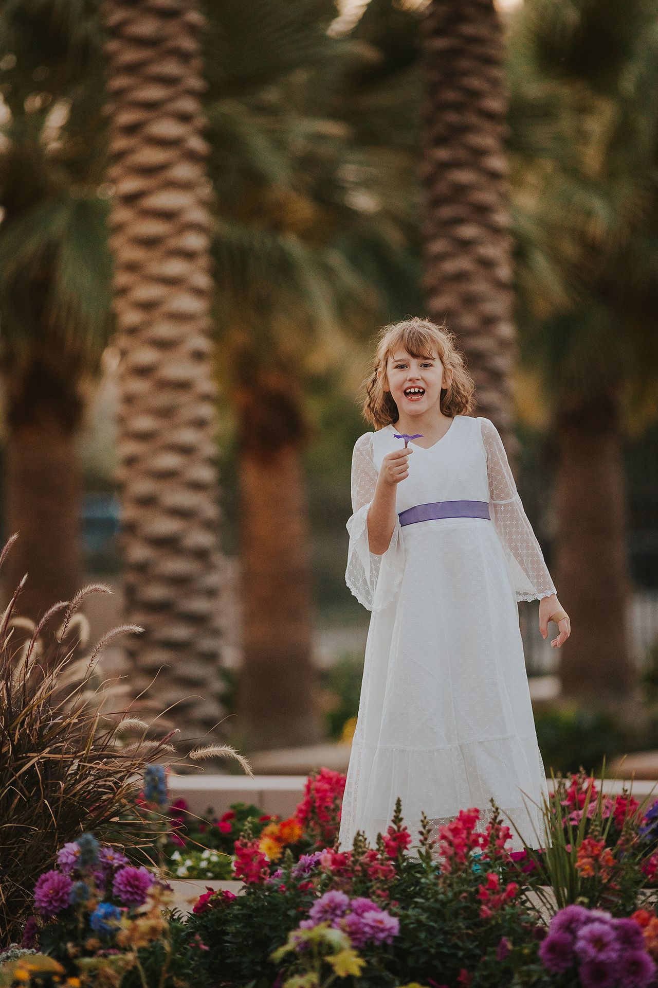 A little girl in a white dress is standing in a garden of flowers.