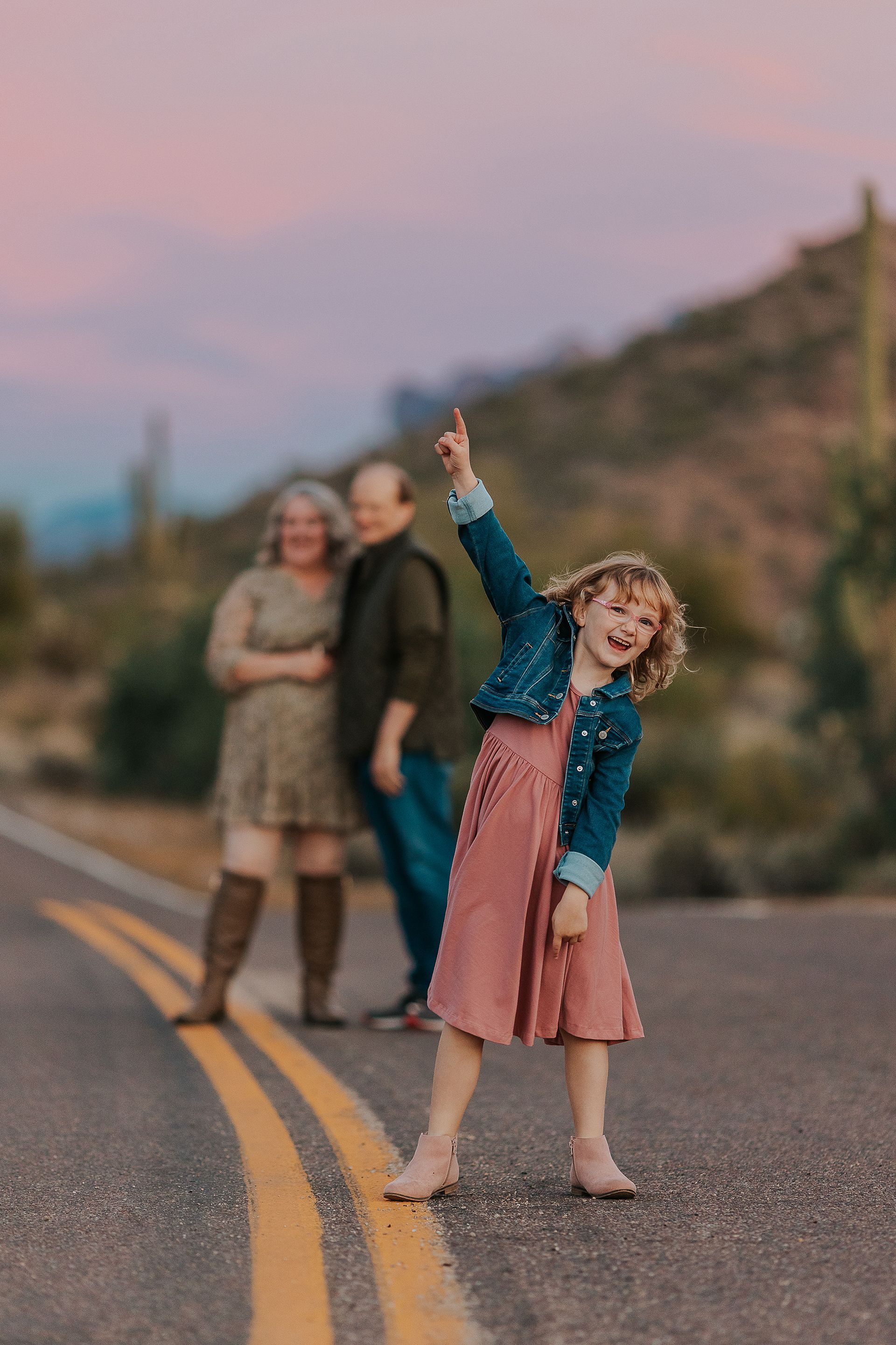 A little girl is standing on the side of a road.