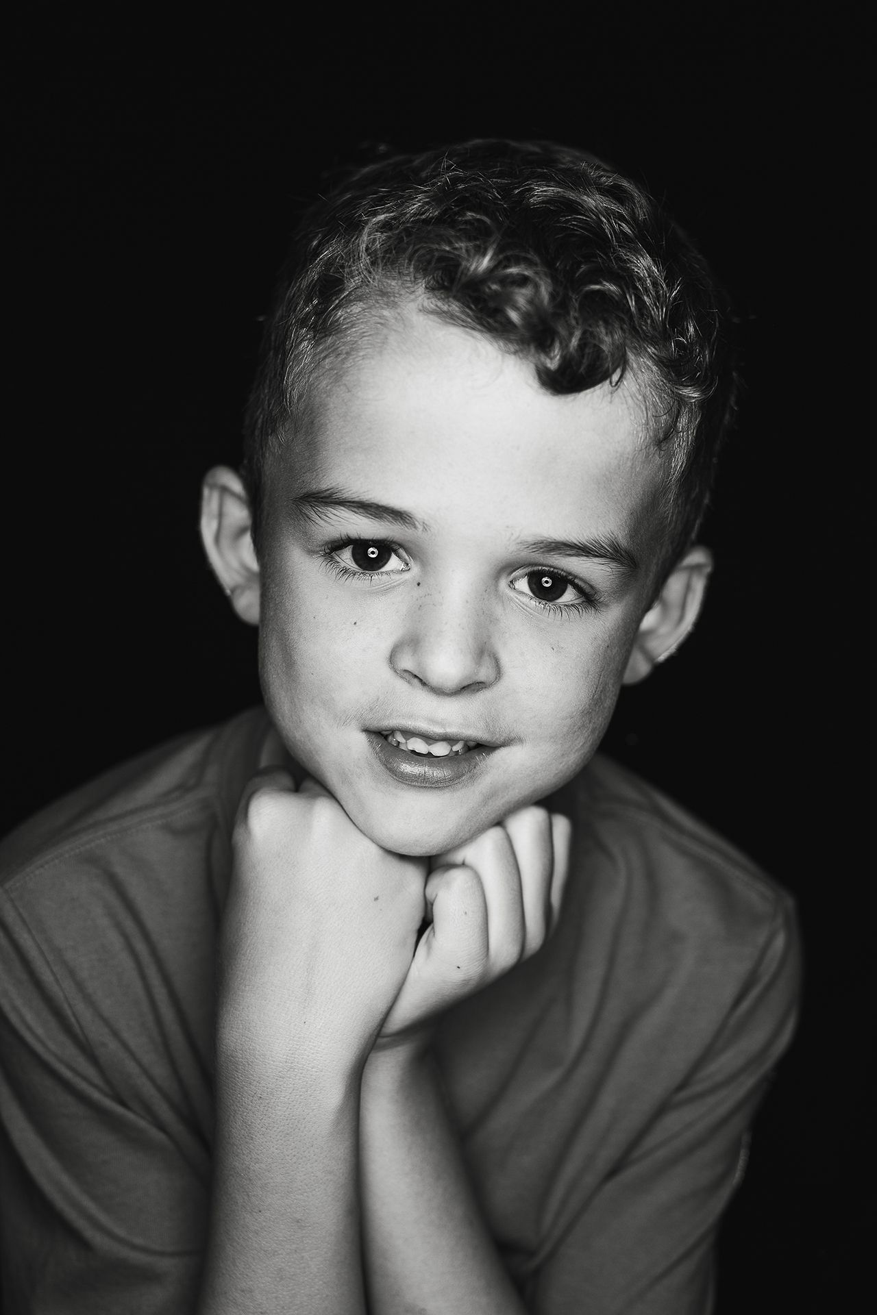 A black and white photo of a young boy with his hand on his chin.