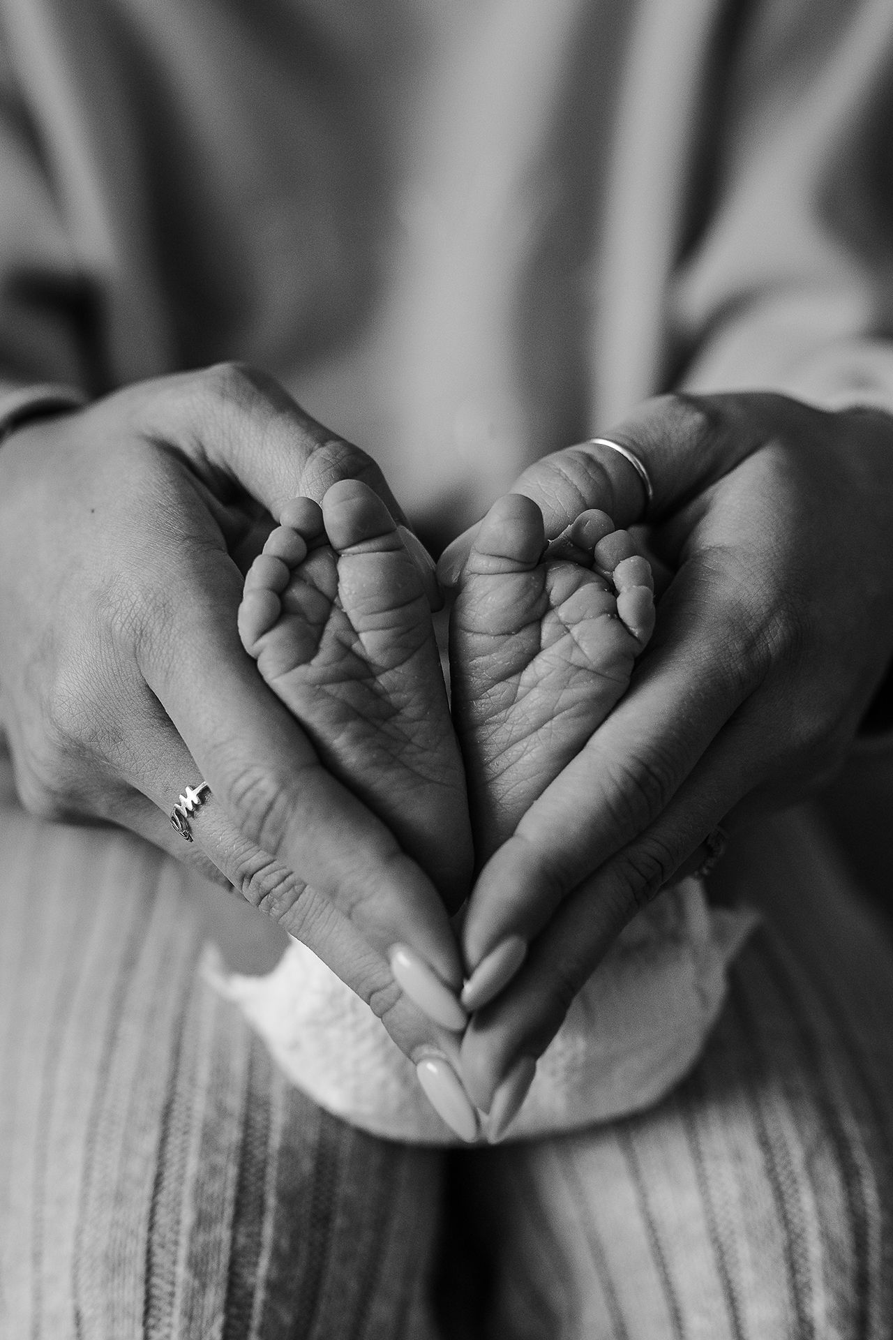 A woman is holding a baby 's feet in her hands in the shape of a heart.