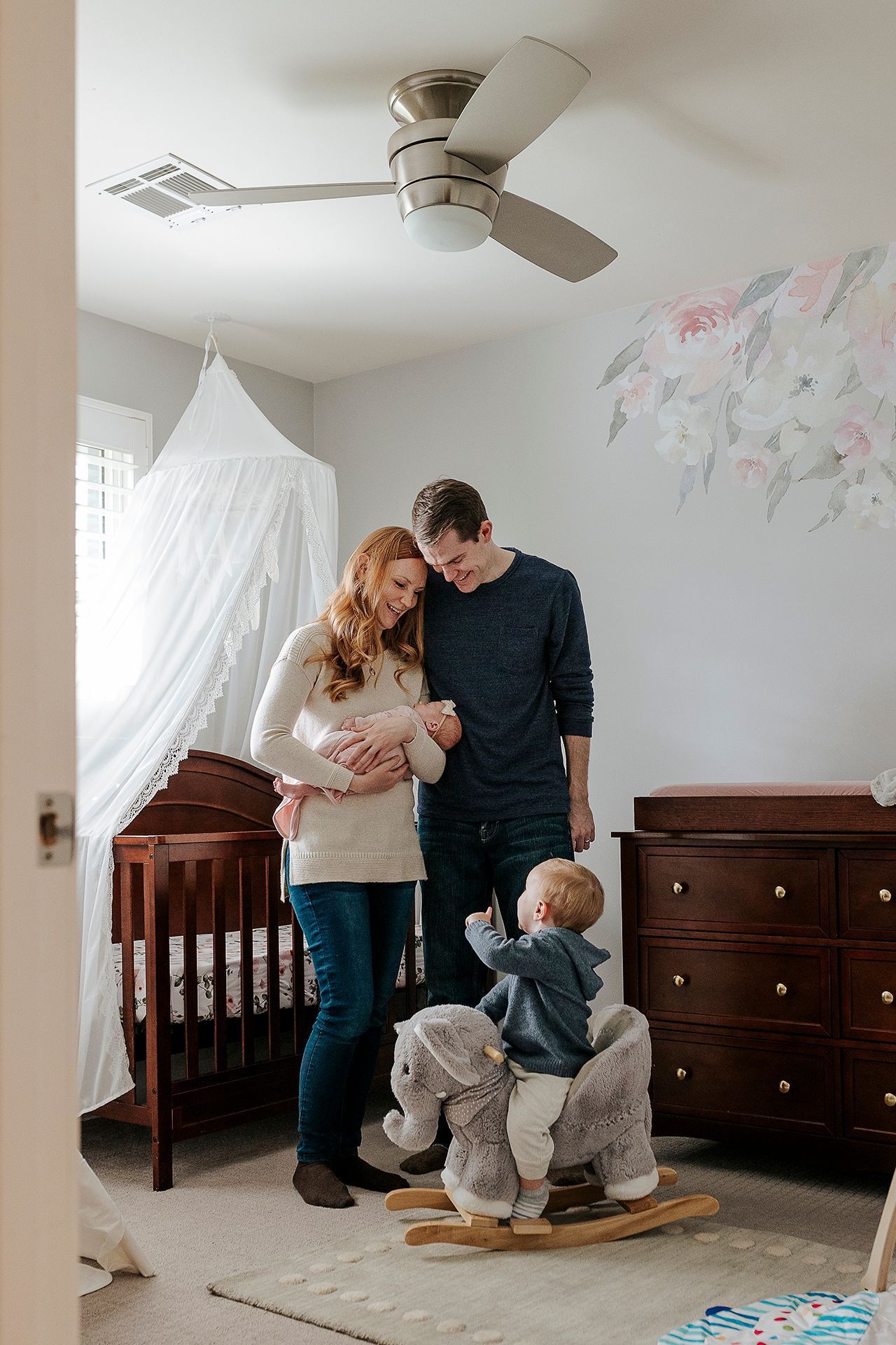 A family is standing in a nursery with a baby and a rocking horse.