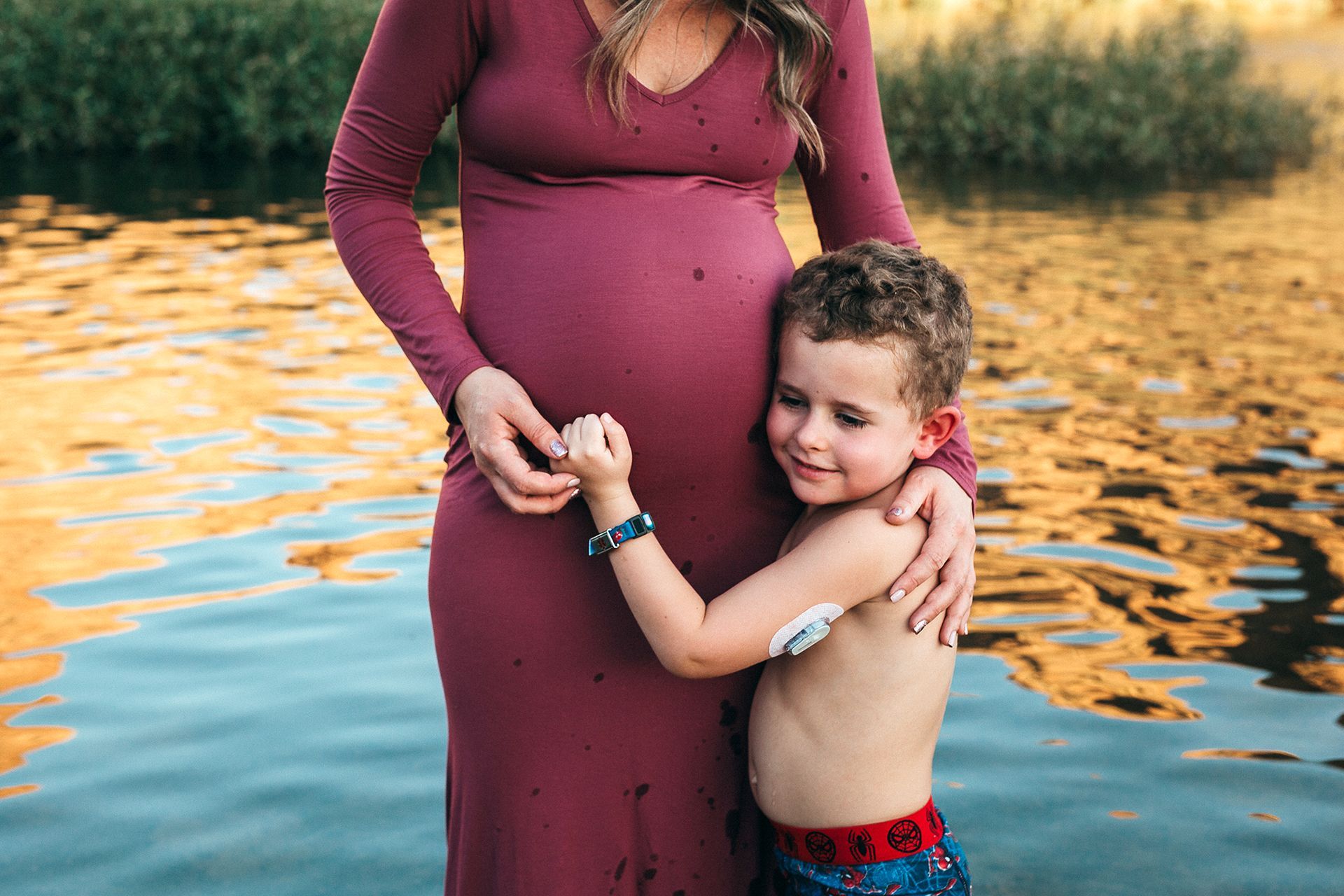 A pregnant woman is standing next to a young boy in the water.