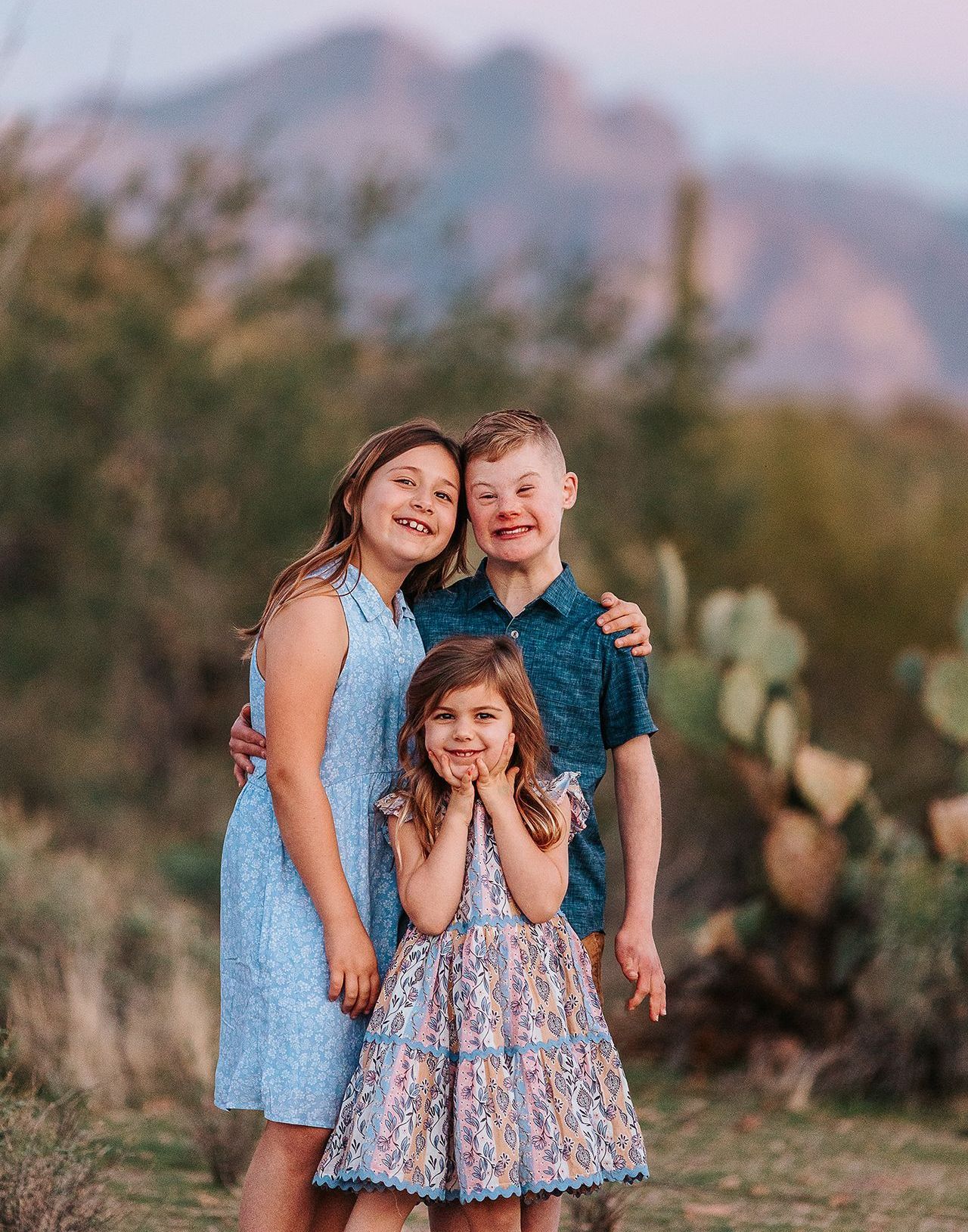 A boy and two girls are posing for a picture in front of a mountain.
