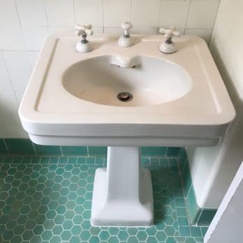 a white sink is sitting on a green tiled floor in a bathroom .