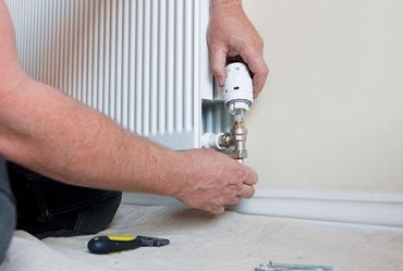 a man is fixing a radiator with a screwdriver