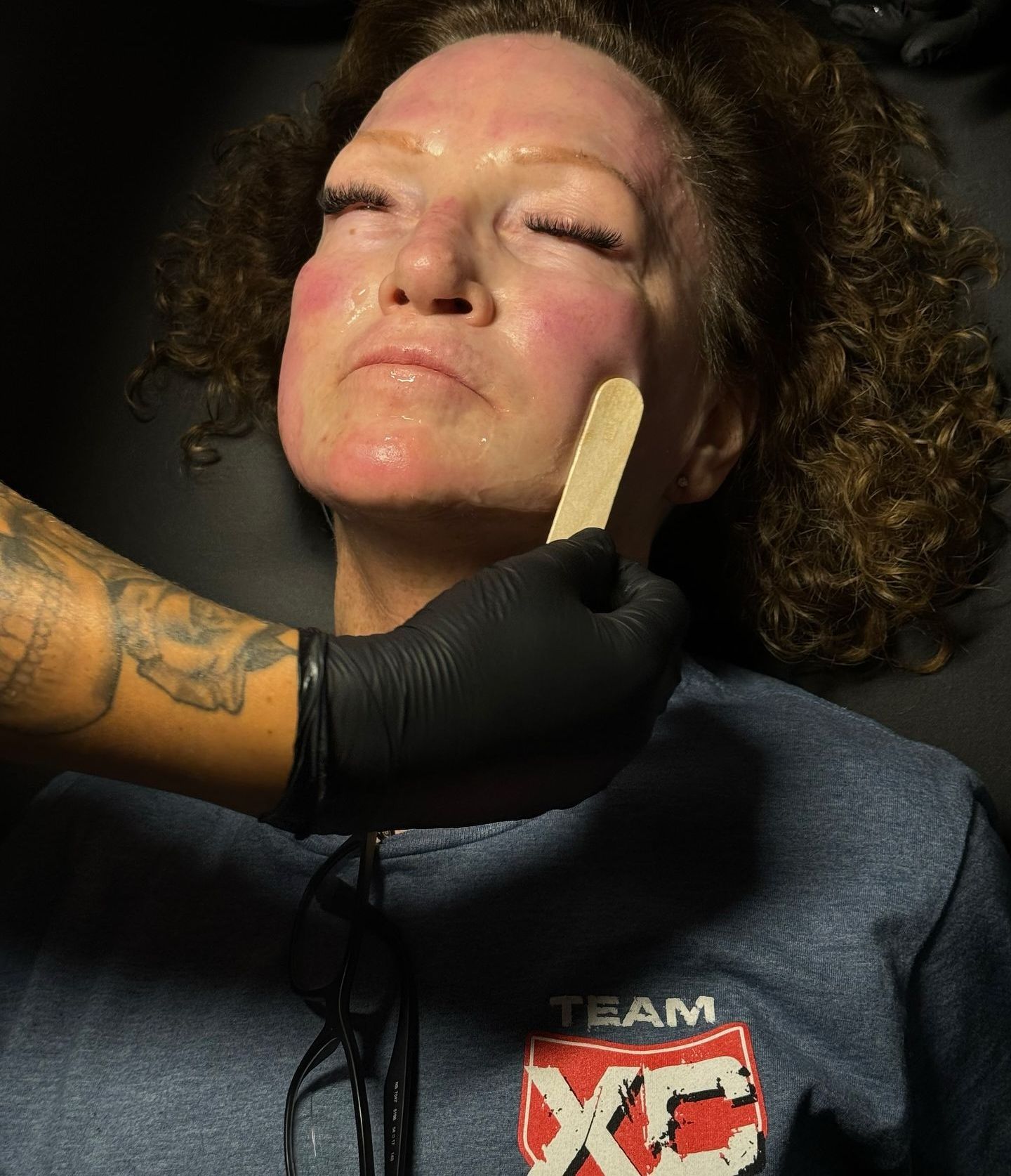 A woman wearing a team xc shirt is getting her face waxed